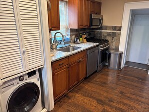 A kitchen with wooden cabinets, a stainless steel microwave, a built-in oven, a dishwasher, and a washing machine. - Cozy Home in SE Washington, DC (Washington)