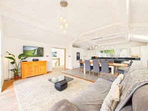 A spacious living area with a sofa, coffee table, and dining table. There is a kitchen in the background with modern appliances. - Steepholm House | Scenic View | Parking | Sleeps 8 (Worcestershire)
