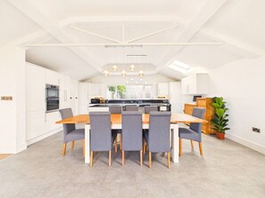 Eine moderne Küche mit weißen Schränken, einer zentralen Kochinsel und einem Essbereich mit Holztisch und grauen Stühlen.