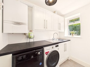 A compact kitchen with a dishwasher, washing machine, and a window with a view of greenery. - Steepholm House | Scenic View | Parking | Sleeps 8 (Worcestershire)