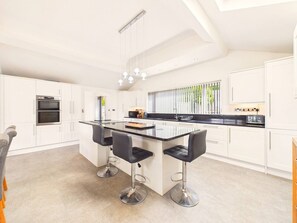 A modern kitchen with a central island, bar stools, and built-in appliances. - Steepholm House | Scenic View | Parking | Sleeps 8 (Worcestershire)