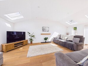 Ein modernes Wohnzimmer mit Flachbildfernseher, grauem Sofa, einer Holzunterhaltungsecke und einem großen Fenster mit Oberlichtern.