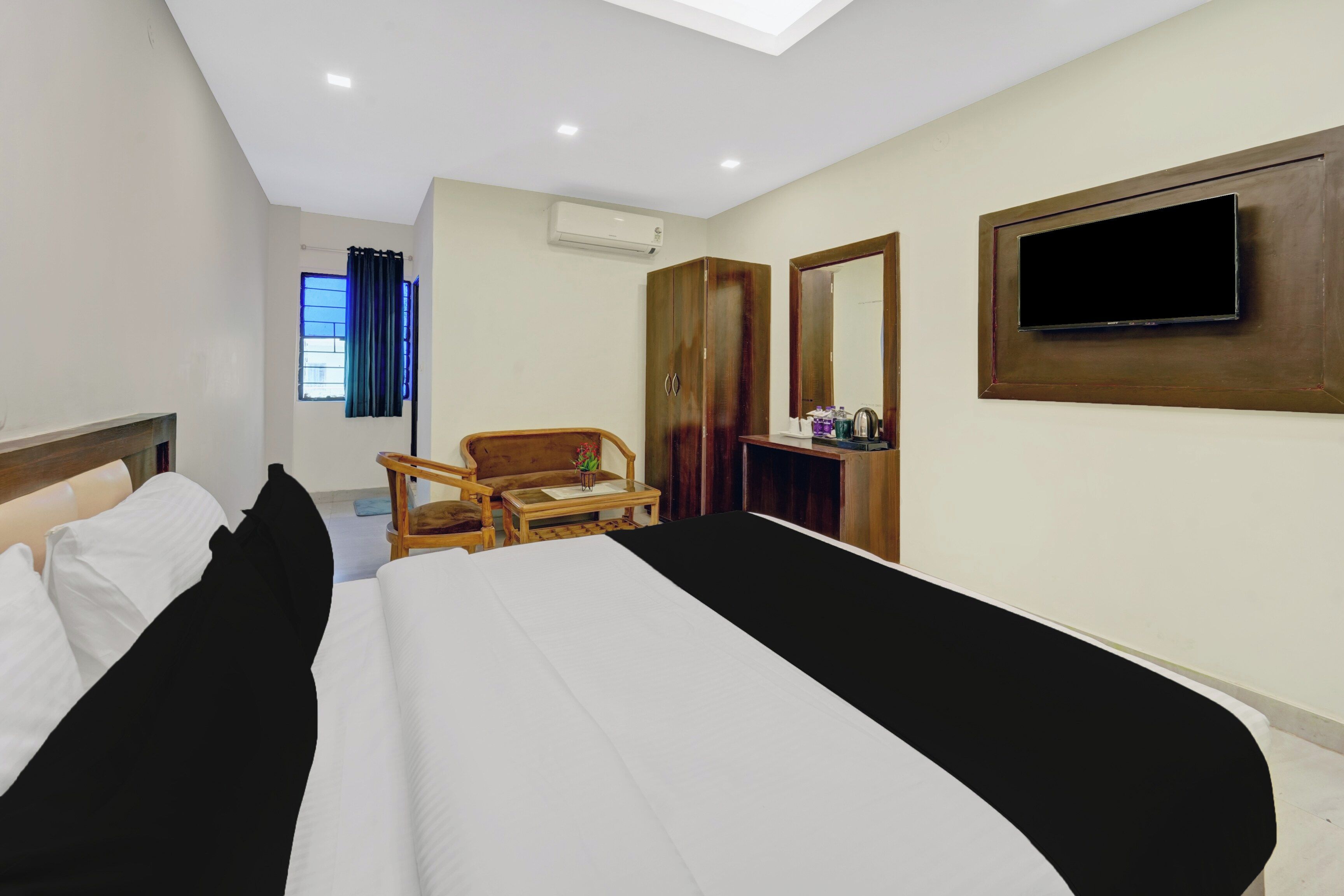 A hotel room with a bed, a desk, a chair, a television, and an air conditioning unit.