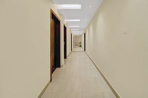 A long, narrow hallway with doors on one side and a potted plant at the end. - Hotel O Le Grande Hotel & Banquet (Patna)
