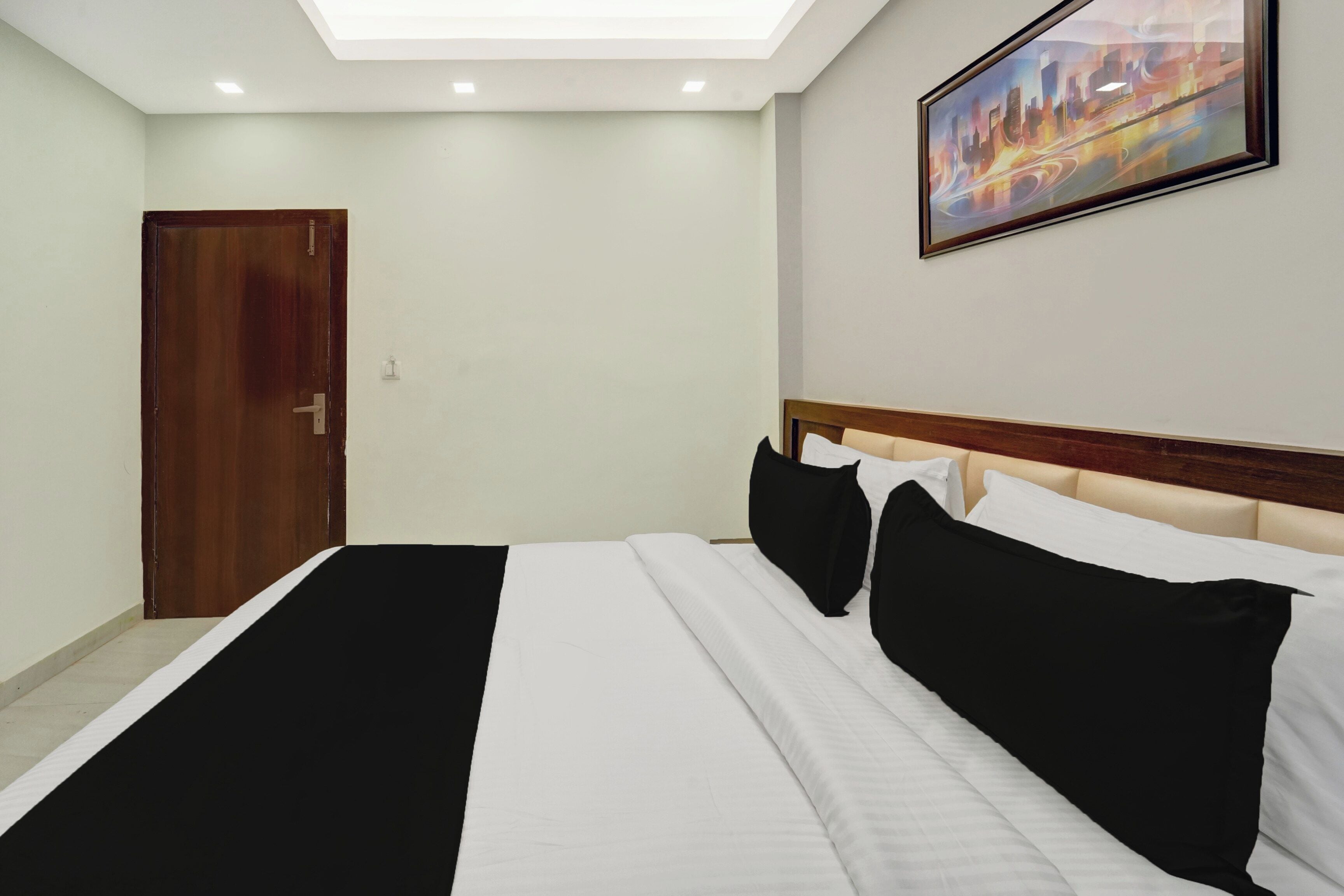 Une chambre d’hôtel avec un lit, une porte, un tableau au mur et un luminaire au plafond.