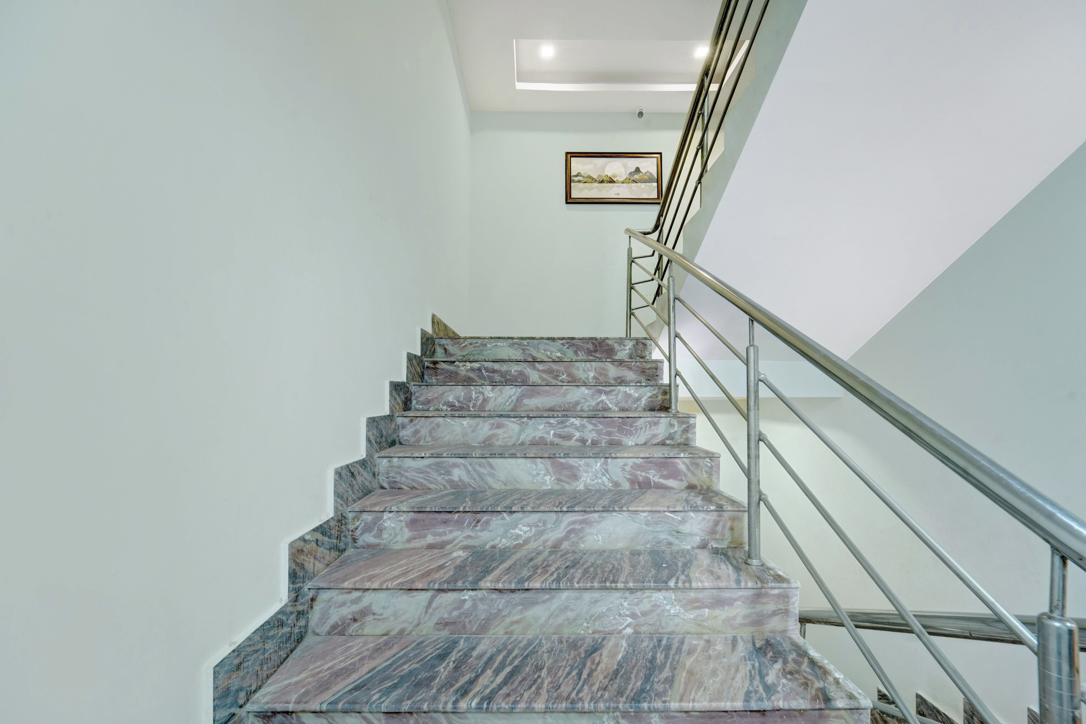 Un escalier en marbre avec une rampe métallique menant à un palier.