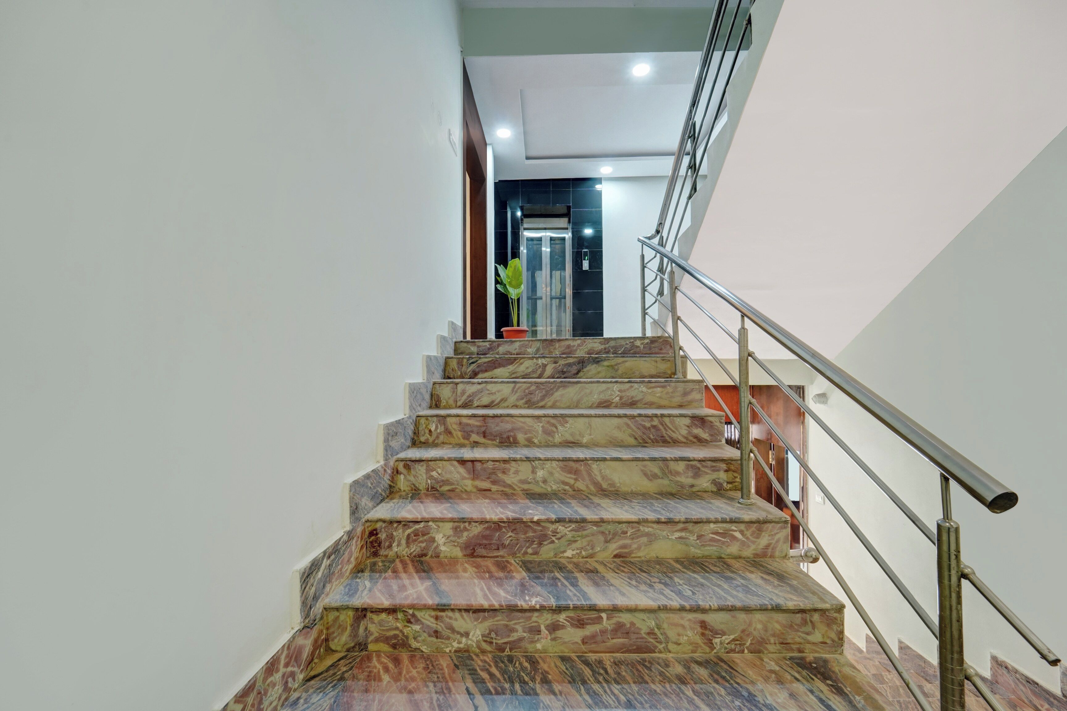 Un escalier en marbre avec des rampes métalliques menant à un ascenseur.
