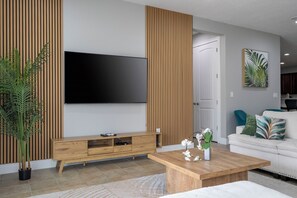 A modern living room with a flat-screen TV, wooden panel accent wall, a white sofa, a coffee table, and a potted plant. - Spacious 11-bedroom house in tranquil Kissimmee with AC (Kissimmee)