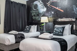 Een hotelkamer met twee bedden, een groot wandtapijt, een lamp en een Star Wars-kussen.