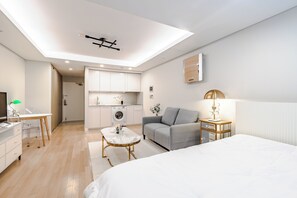 Una habitación moderna y bien iluminada con cama, sofá, mesa de comedor y zona de cocina.