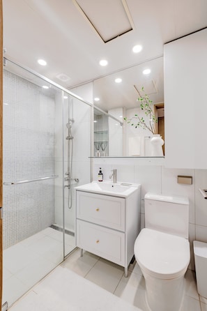 A modern bathroom with a glass-enclosed shower, a white sink with a mirror above, and a toilet. - Welcome to Your Home in the Heart of Seoul! (Jongno-gu)