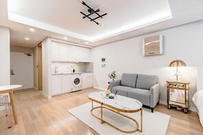 En moderne lejlighed med et køkken, en grå sofa, et marmorbord og et lille sofabord med en lampe.