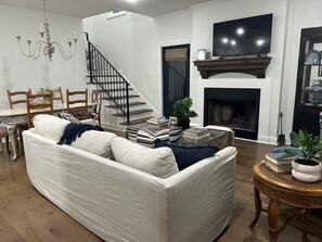 A living room with a sofa, a coffee table, a fireplace, a television, and a staircase. - Charming 3 bedroom home in Oxford. Located 3.3 miles from the Square and Grove. (Oxford)