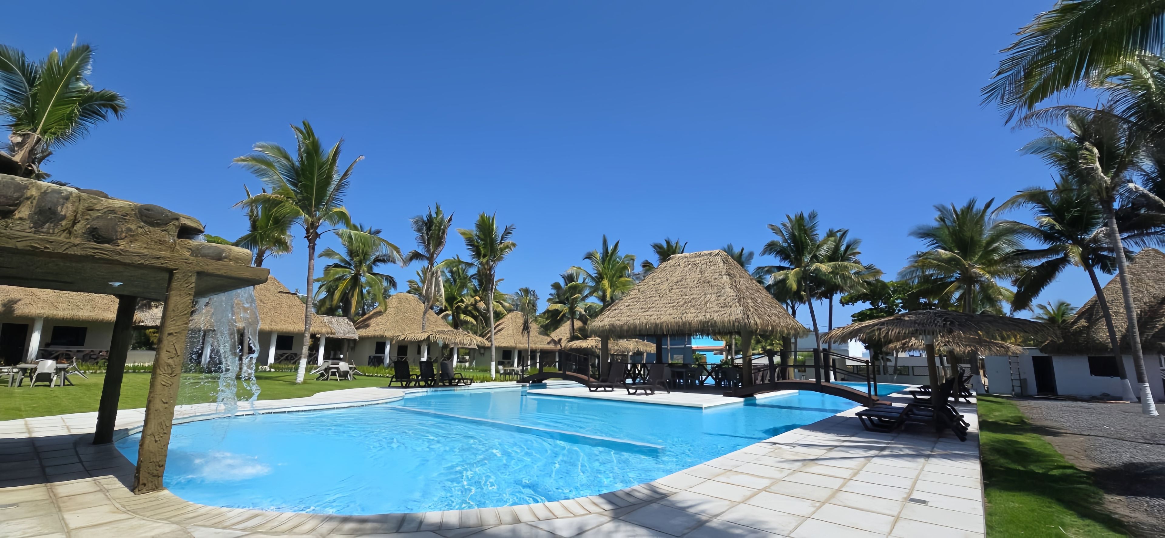 A pool area with thatched-roof structures and palm trees.