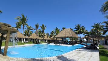 A pool area with thatched-roof structures and palm trees.