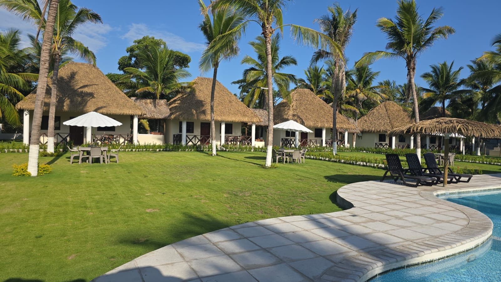 Un complexe hôtelier doté de villas aux toits de chaume, d’une piscine et de palmiers.