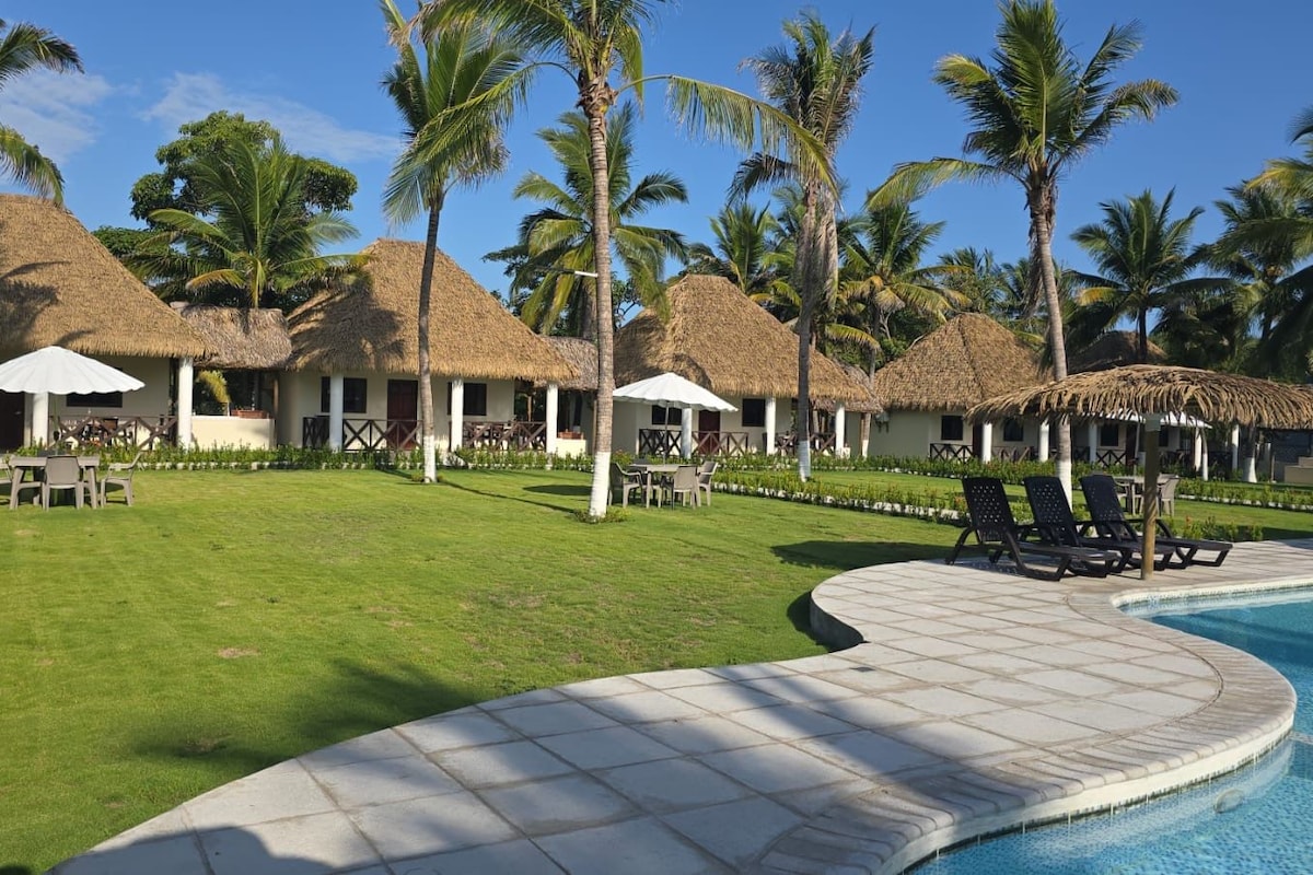 A resort with thatched-roof villas, a swimming pool, and palm trees.
