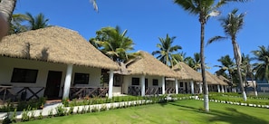 A row of thatched-roof cottages with white walls, surrounded by well-maintained lawns and palm trees. - Hotel El Marinero (Chiquimulilla)