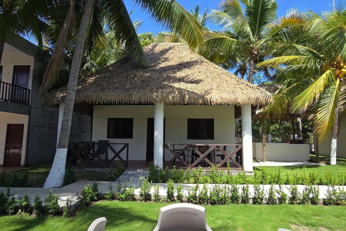 A resort with thatched-roof structures, palm trees, and a well-maintained lawn.