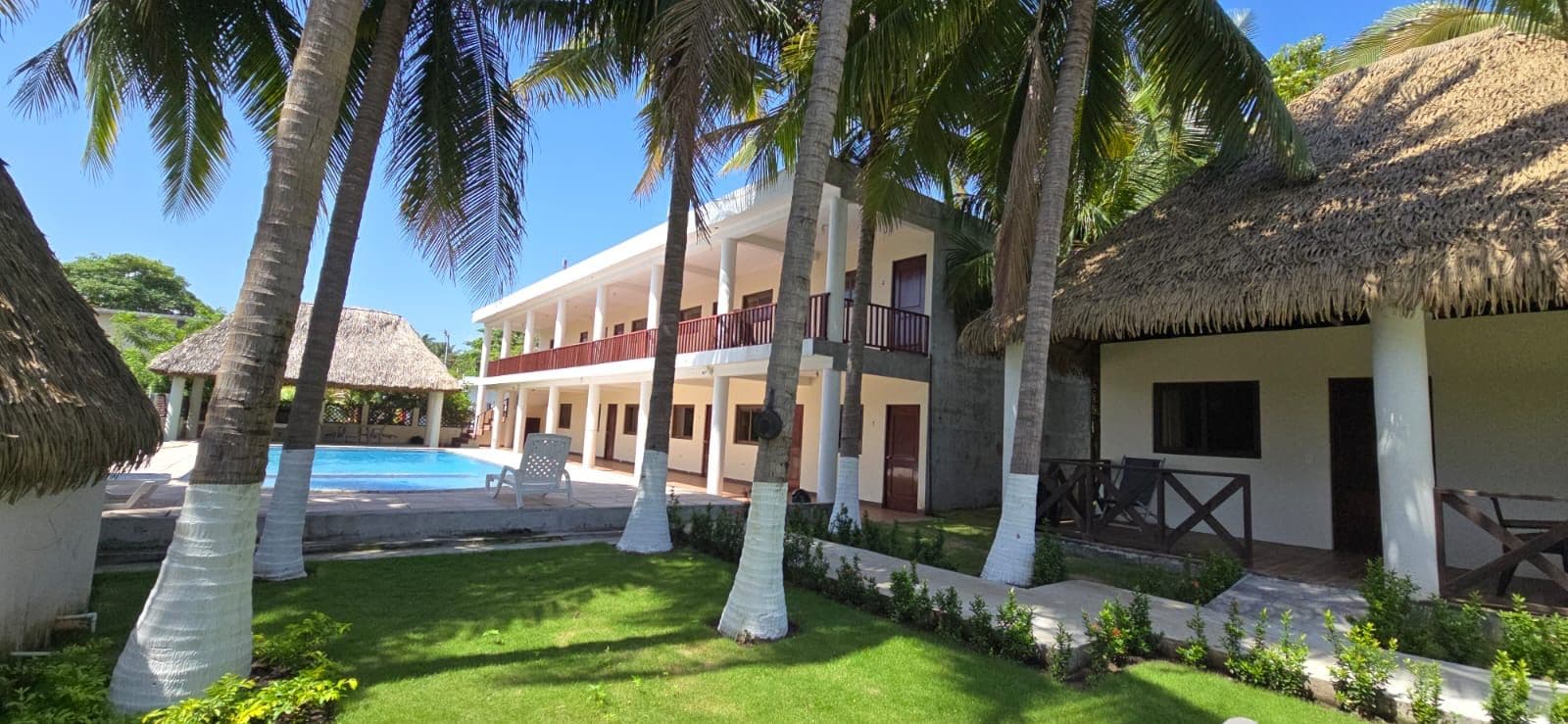 Un resort con piscina, palmeras y un edificio de techo de paja.