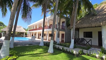 Un resort con piscina, palmeras y un edificio de techo de paja.