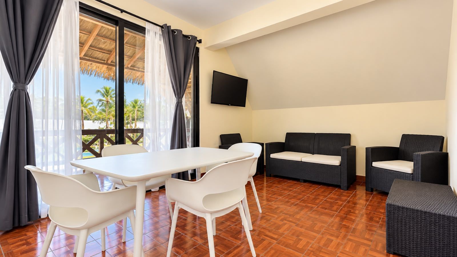 A room with a dining table and chairs, a sofa, and a TV on the wall.