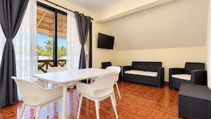 A room with a dining table and chairs, a sofa, and a TV on the wall.