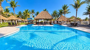 Una piscina con sillones de descanso y estructuras de techo de paja.