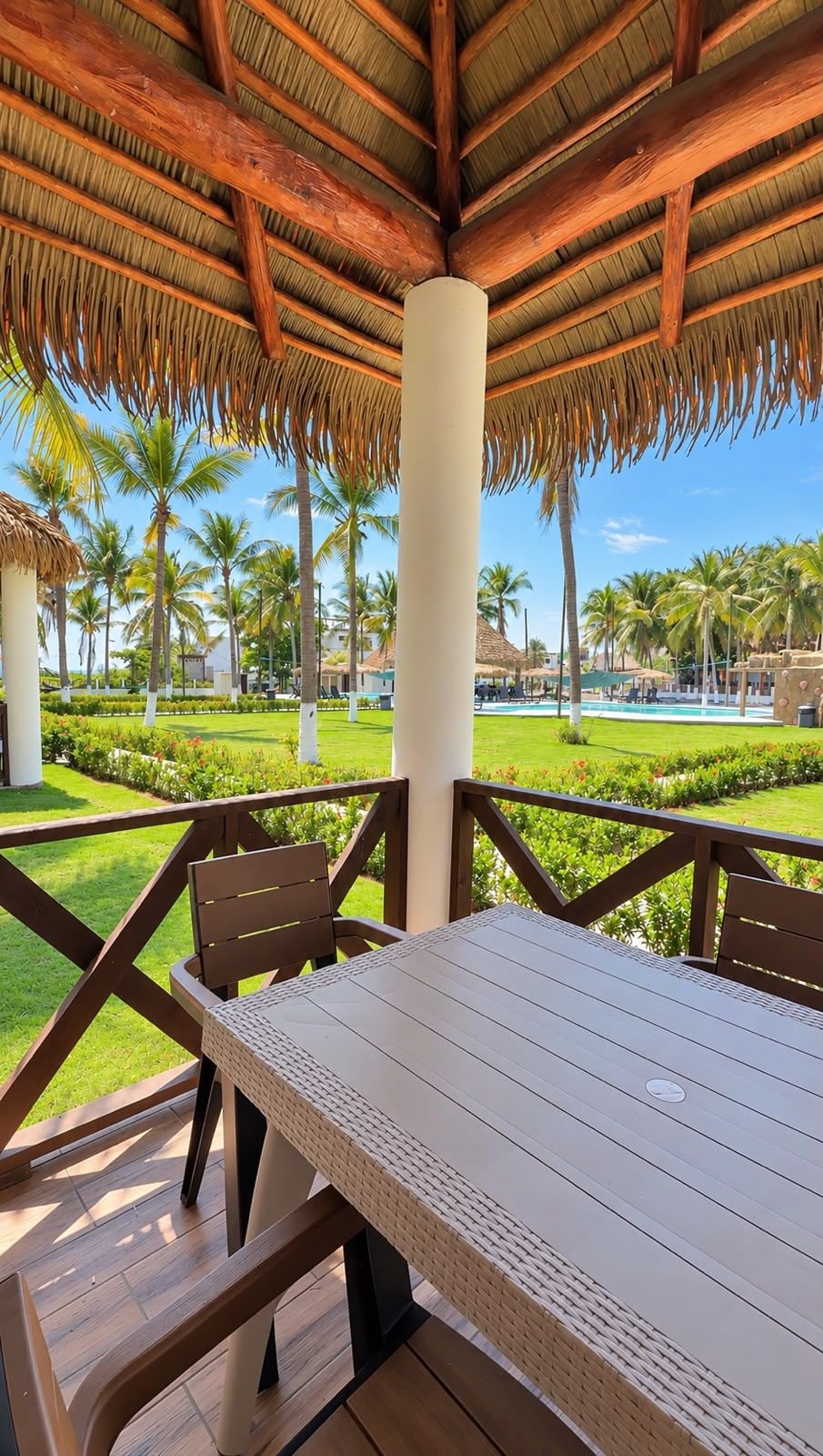 Un espace extérieur aménagé, abrité et doté d’une table et de chaises, offrant une vue sur une piscine et des palmiers.