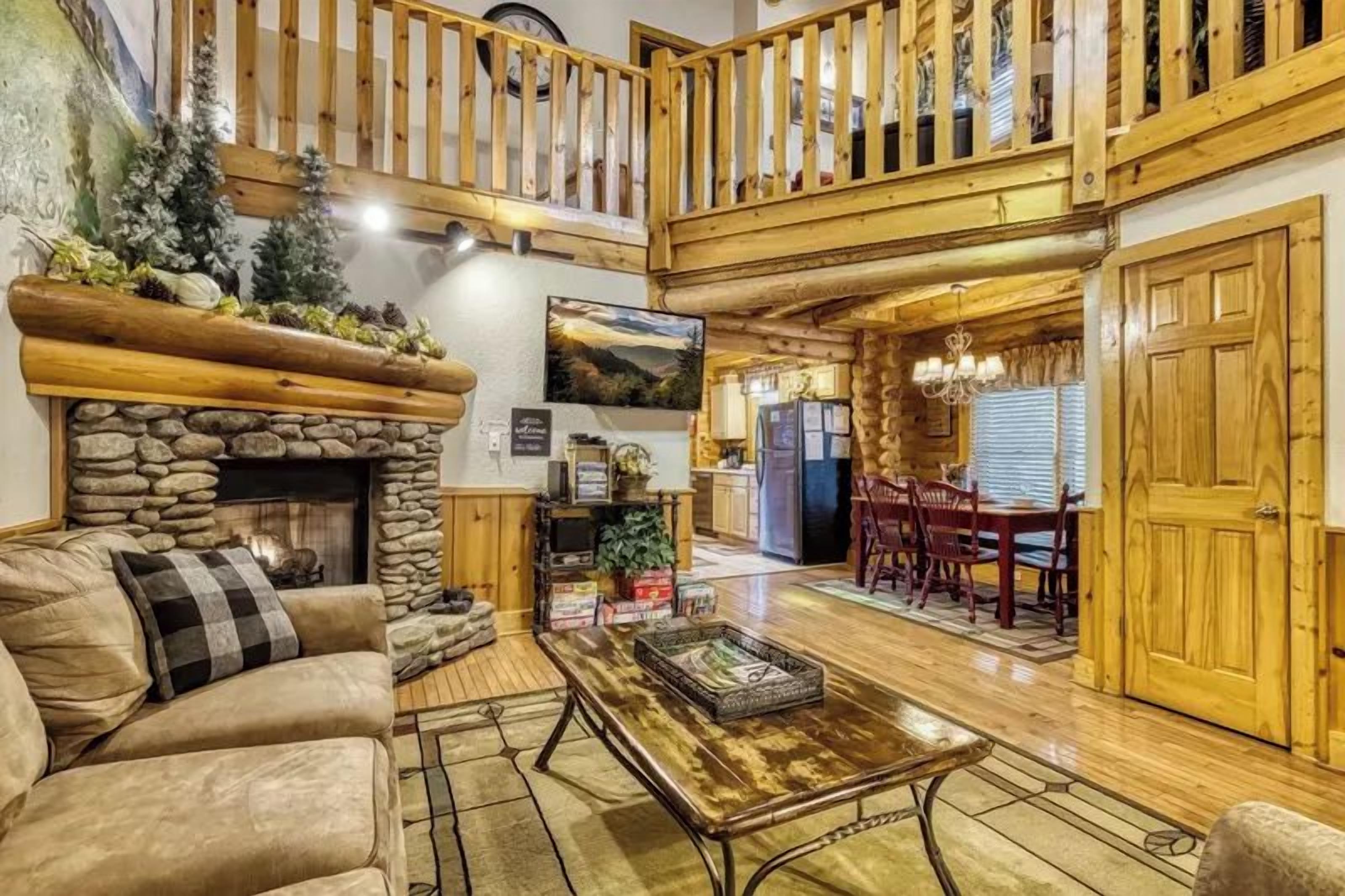 A cozy interior with a stone fireplace, wooden furniture, and a dining area with a high ceiling and wooden railing.
