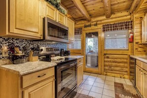 A kitchen with wooden cabinets, a microwave, a stove, and a window with blinds. - Cabin in Pigeon Forge - Welcome to Lucky Logs! (Pigeon Forge)