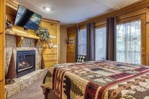 A cozy room with a stone fireplace, a television mounted on the wall, and a large bed with a quilt. - Cabin in Pigeon Forge - Welcome to Lucky Logs! (Pigeon Forge)