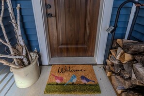 A wooden door with a doormat, a potted plant, and a stack of firewood. - Beautiful cozy 2-bedroom cottage with a woodburning stove and AC in Duluth (Duluth)