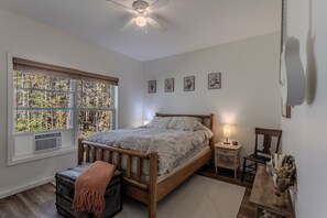Ein Schlafzimmer mit einem hölzernen Bett, einem Nachttisch, einem Stuhl, einem Fenster mit Jalousien und einem Deckenventilator.