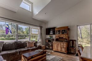 A spacious living room with a sofa, coffee table, wooden cabinet, and large windows offering a view of the outdoors.