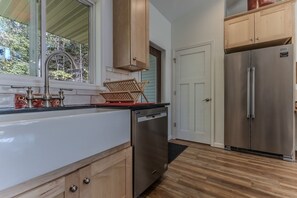 A kitchen with a stainless steel refrigerator, wooden cabinets, a dishwasher, and a window with a view of trees. - Beautiful cozy 2-bedroom cottage with a woodburning stove and AC in Duluth (Duluth)