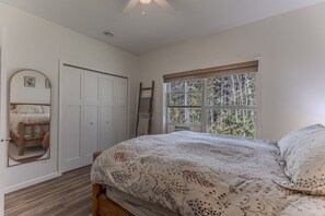 A bedroom with a bed, a window with a view of trees, a white wardrobe, and a ladder leaning against the wall.