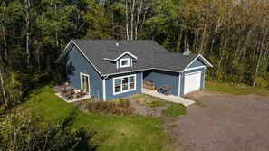 A two-story house with a garage, surrounded by a well-maintained lawn and dense forest.