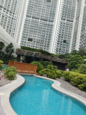 A swimming pool with a tiled edge, surrounded by greenery and a wooden deck. - Hotel Residences at Acqua- Novotel Suites (Mandaluyong City)