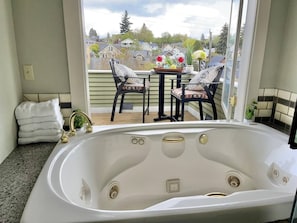 Une salle de bain avec une grande baignoire, une fenêtre et une vue sur un balcon agrémenté de chaises et d’une table.