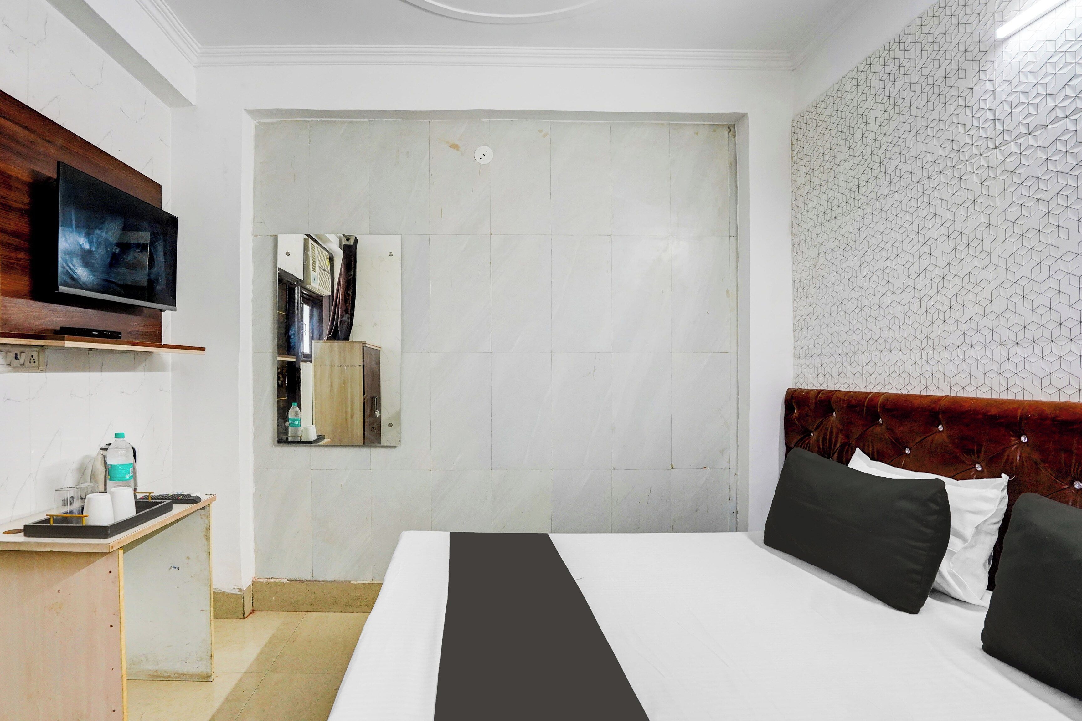 Een hotelkamer met een bed, een televisie, een klein bureau met een waterfles en een spiegel.
