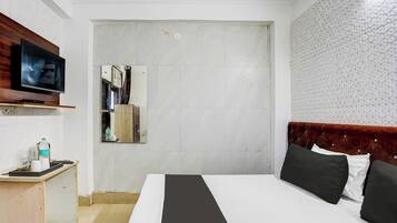 Een hotelkamer met een bed, een televisie, een klein bureau met een waterfles en een spiegel.