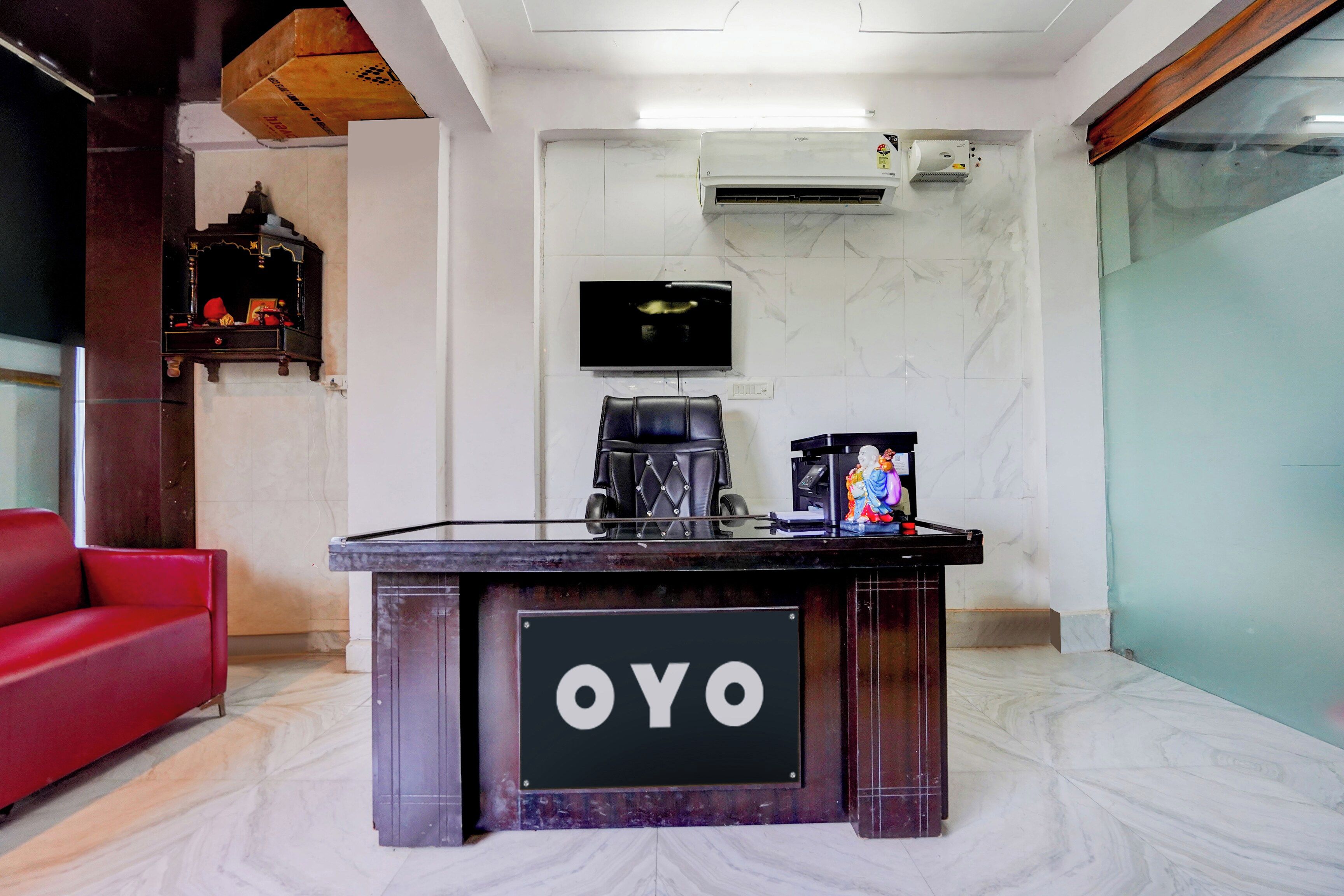 Una recepción con un cartel que dice 'OYO' en el vestíbulo de un hotel, con un sofá rojo, suelo de mármol y una unidad de aire acondicionado en la pared.