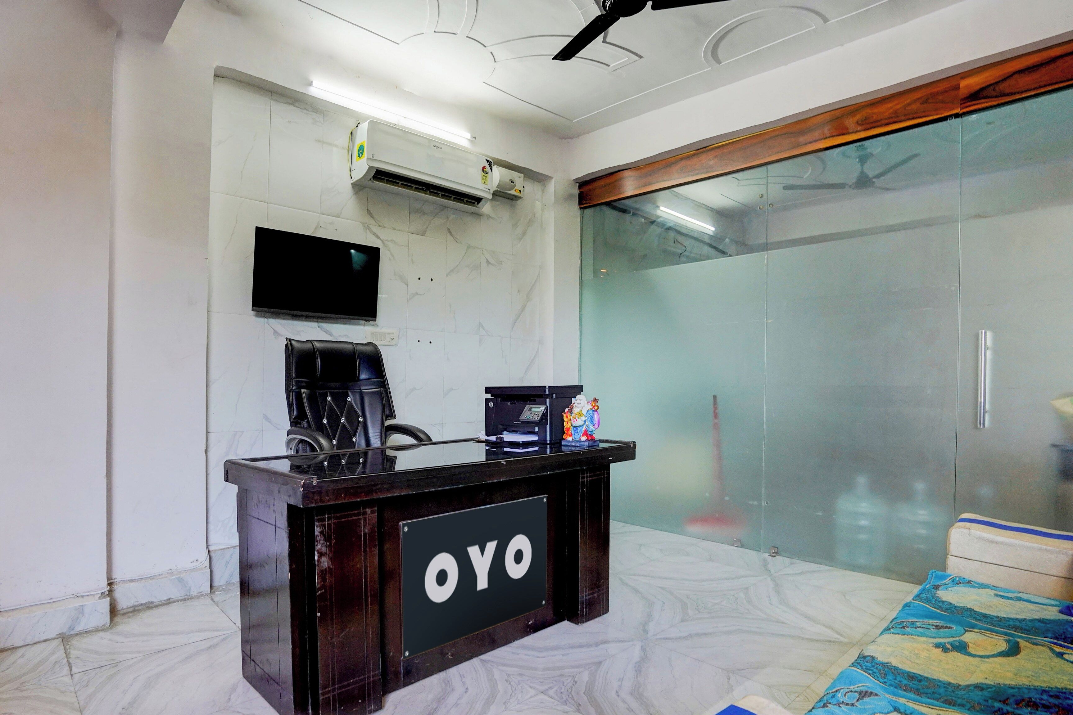 Una mesa de recepción con un cartel que dice 'OYO', un televisor de pantalla plana montado en la pared y un ventilador de techo.