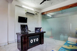 Una mesa de recepción con un cartel que dice 'OYO', un televisor de pantalla plana montado en la pared y un ventilador de techo.