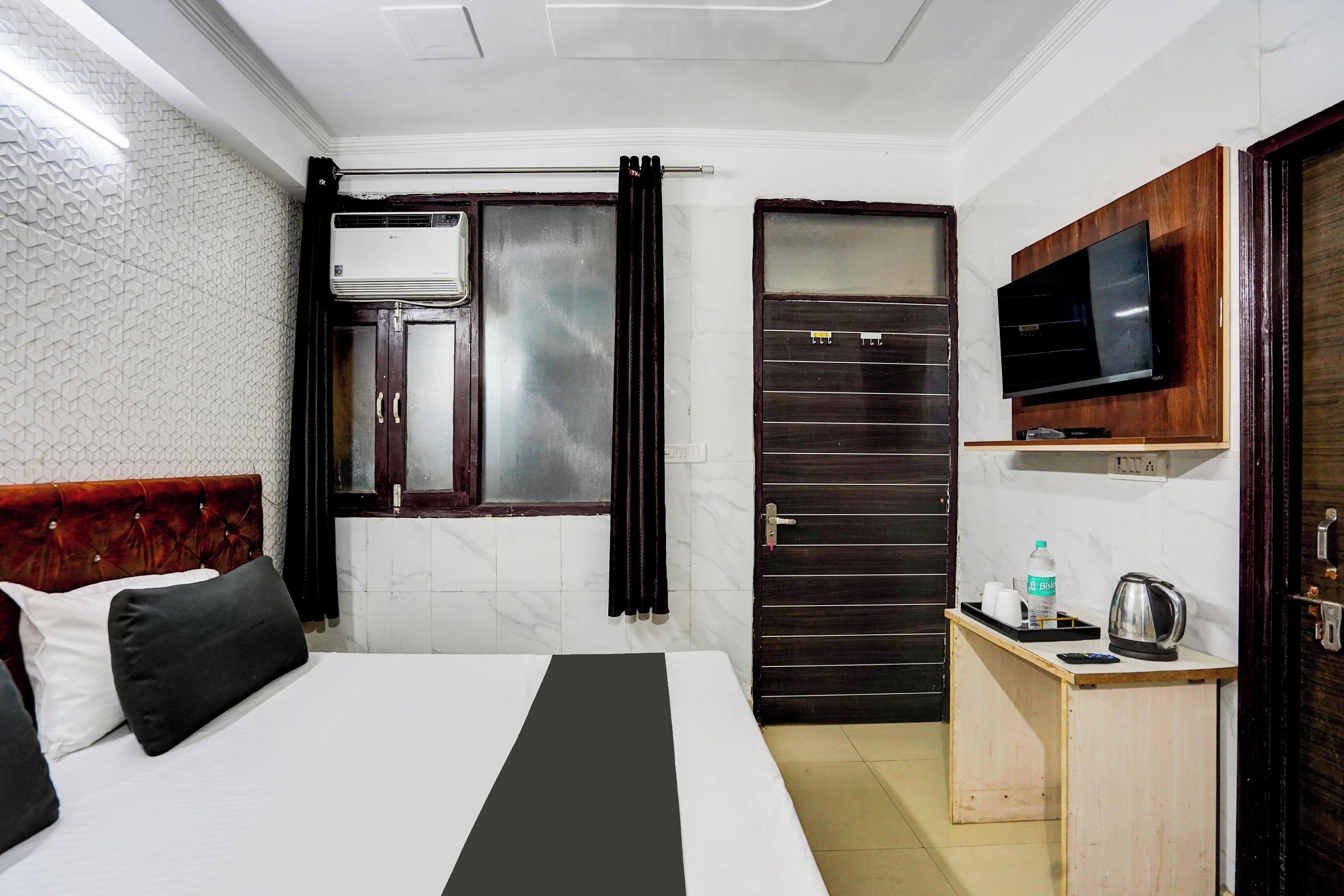 A hotel room with a bed, a TV, a small table with a kettle, and a cabinet.