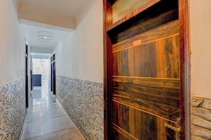 A corridor with a stone wall on one side and a wooden door on the other. - Hotel O The Maruti hotel (Noida)