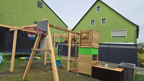 A wooden play structure with a swing set and a basketball hoop in a backyard. - Worker's Apartment & Family Home with Sauna in Colmberg (Colmberg)