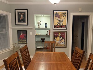 Un comedor con una mesa y sillas de madera, rodeado de carteles enmarcados y una estantería.