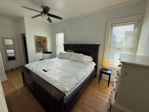 Un dormitorio con una cama grande, un ventilador de techo, una mesita de noche con lámpara y un aparador.